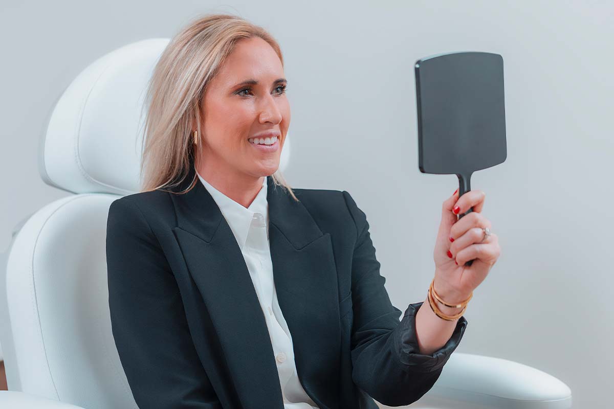 Woman reviewing facelift results in a handheld mirror at Vida Bela Plastic Surgery